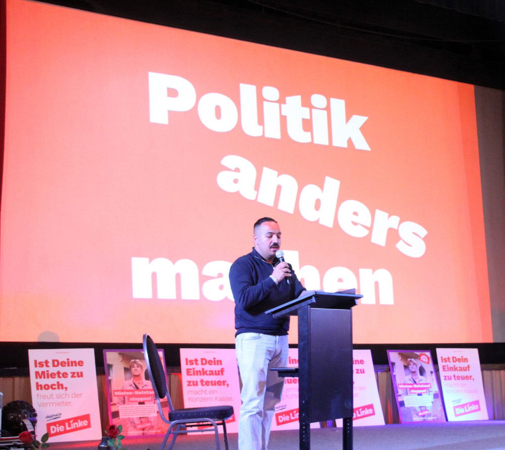 Mustafa redet bei der Nachbarschaftsversammlung in seinem Wahlkreis. Im Hintergrund Plakate mit den Forderungen aus der Nachbarschaft, zum Beispiel nach einem bezahlbaren Leben. Und der Spruch "Politik anders machen"