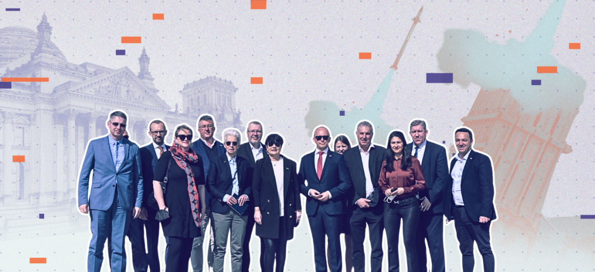 Auf dem Bild zu sehen: Eine Gruppe an Personen, vor allem Bundestagsabgeordnete, die in die Kamera sehen. Im Hintergrund stilisiert der Bundestag und eine Rakete.