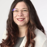 Regine Neuweiler-Tran Portraitfoto von vorne, weiblich, Brille, lange braune Haare in Locken frisiert, lächelnd.
