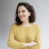 Delara Burkhardt Auf dem Bild ist mittig Delara mit verschränkten Armen vor einem neutralen Hintergrund zu sehen