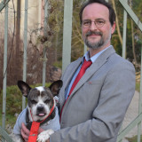 Dr. Michael Daub mit Hund Pepo auf dem Arm, beide in grauem Anzug und roter Krawatte gekleidet.