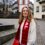 Katrin Fey Ich stehe in der Oberstadt Siegen vor der bekannten Nikolaikirche. Um meinen Hals trage ich einen schönen roten Schal der Linken.