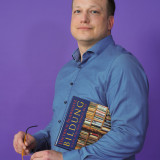 Hendrik Schäfer Hendrik Schäfer steht vor violettem Hintergrund und hält ein Buch in der Hand.