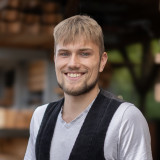 Lars Biesenthal Lars Biesenthal zusehen in seiner Zimmerkluft, vor einem Holzlager.