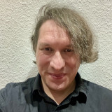 Bente Pieck Ein Mann mit mittellangem Haar und schwarzem Hemd lächelt in die Kamera