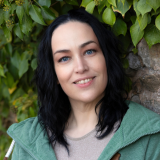 Portraitfoto von Katja Daish vor Naturhintergrund, sie lächelt.