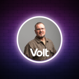 Heiko Kunz Kandidat Heiko trägt ein kariertes Hemd in Erdfarbtönen, um ihn herum ein weißer Kreis und die Aufschrift Volt. Der Hintergrund ist lila und beinhaltet eine Brandmauer.