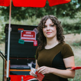 Ein Foto von Anne Helm im Freien vor einem Infostand, freundlich offen schauend und bereit für ein Gespräch
