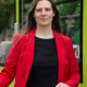 Madeleine Linke Eine junge Frau steht mit einem Fahrrad vor einer Straßenbahn der Magdeburger Verkehrsbetriebe. Sie trägt ein rotes Sakko und ein schwarzes T-Shirt. Die langen Haare sind offen.