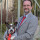 Dr. Michael Daub mit Hund Pepo auf dem Arm, beide in grauem Anzug und roter Krawatte gekleidet.