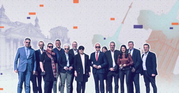 Auf dem Bild zu sehen: Eine Gruppe an Personen, vor allem Bundestagsabgeordnete, die in die Kamera sehen. Im Hintergrund stilisiert der Bundestag und eine Rakete.