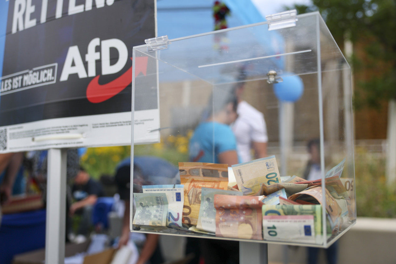 Eine Spendenbox steht neben dem AfD-Logo an einem Infostand der Partei für die Landtagswahl in Sachsen-Anhalt im Kurpark.