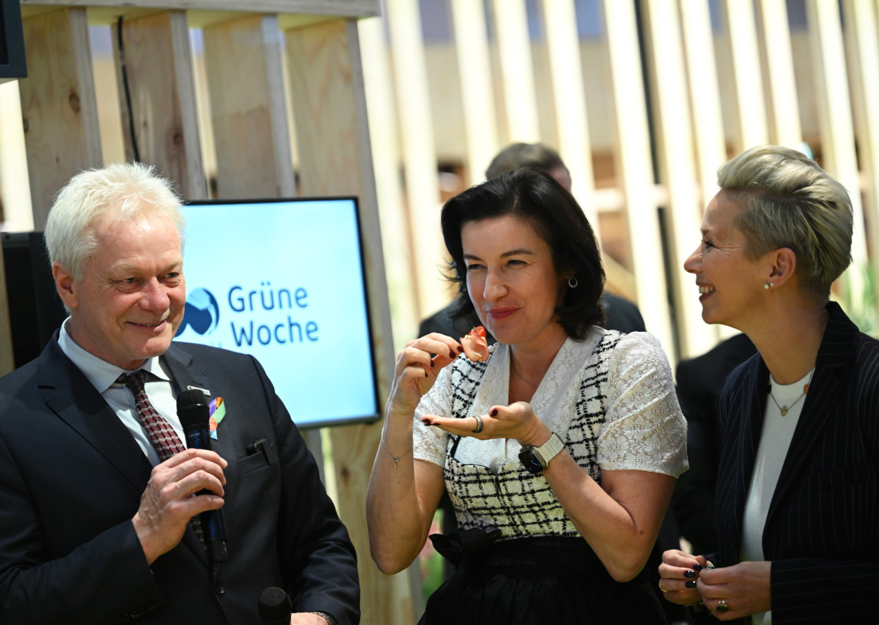 Dorothee Bar steht neben Alois Rainer auf der Grünen Woche, hält ein Häppchen in der Hand und lächelt 